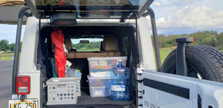 White Jeep's rear cargo area open, neatly packed with travel essentials: storage bins, water, & gear. Perfect for RV rental.