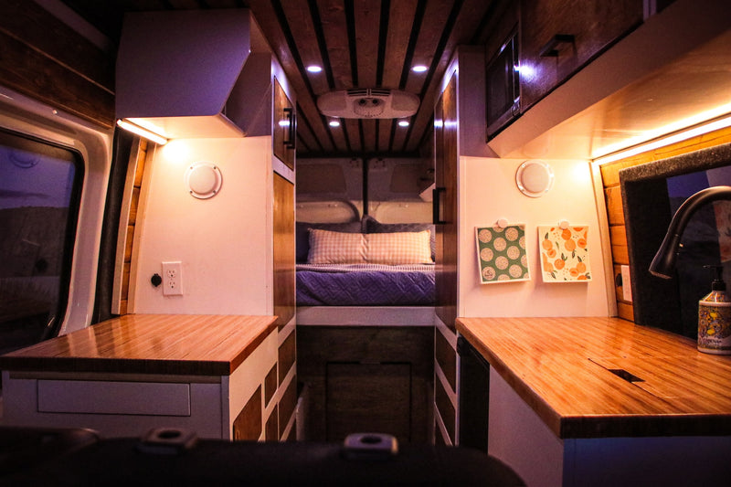 Explore this cozy rv rental campervan interior. Features warm lighting, wooden countertops, and a bed in the rear for comfortable travel. — photo 5