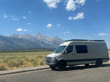 Grey Mercedes Sprinter RV rental van overlooks Grand Teton mountains on a sunny day. Adventure awaits!