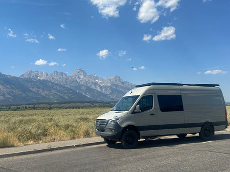 Grey Mercedes Sprinter RV rental van overlooks Grand Teton mountains on a sunny day. Adventure awaits!
