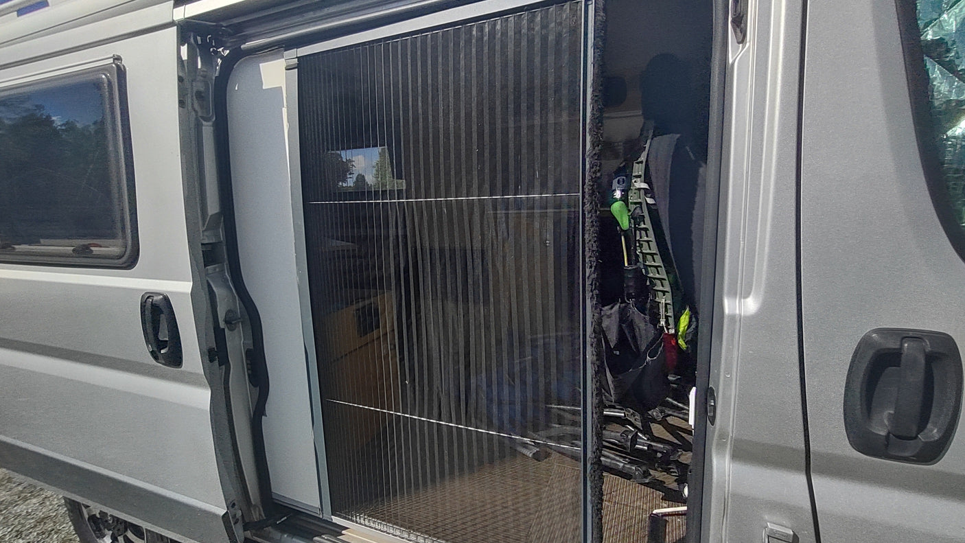 RV rental camper van with open side door and extended pleated mosquito net. A bicycle and textured flooring are visible inside.