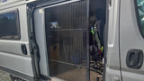 RV rental camper van with open side door and extended pleated mosquito net. A bicycle and textured flooring are visible inside.