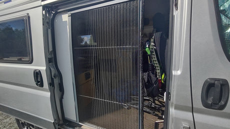 RV rental camper van with open side door and extended pleated mosquito net. A bicycle and textured flooring are visible inside.