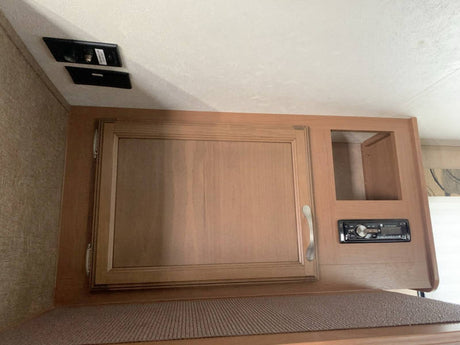 RV rental: Overhead light wood cabinet with door, open cubby, and built-in stereo system for entertainment setup.