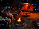 A group enjoys a night by the warm campfire, parked next to their bright orange FreeSolo RV rental at a campground.