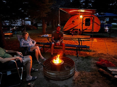 A group enjoys a night by the warm campfire, parked next to their bright orange FreeSolo RV rental at a campground.