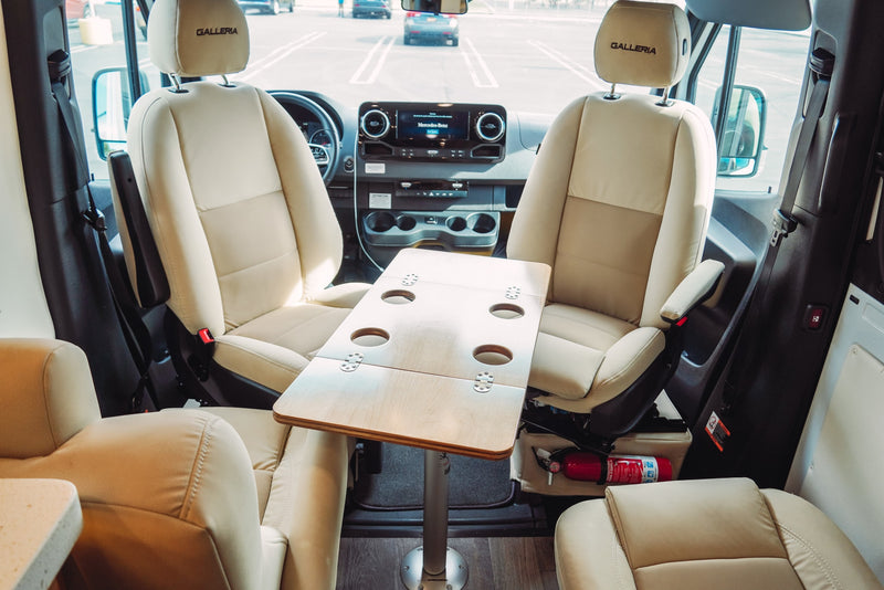 Spacious RV rental interior: cream swiveling front seats, a central table with cup holders, and a Mercedes-Benz dashboard for comfort. — photo 3
