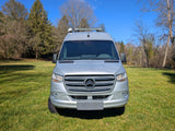 Front view of a silver Mercedes Sprinter van, perfect for **rv rental**, parked in a sunny grassy field.