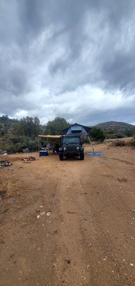 An overlanding Jeep with rooftop tent & awning setup at a dirt campsite. A robust RV rental alternative for outdoor adventure.
