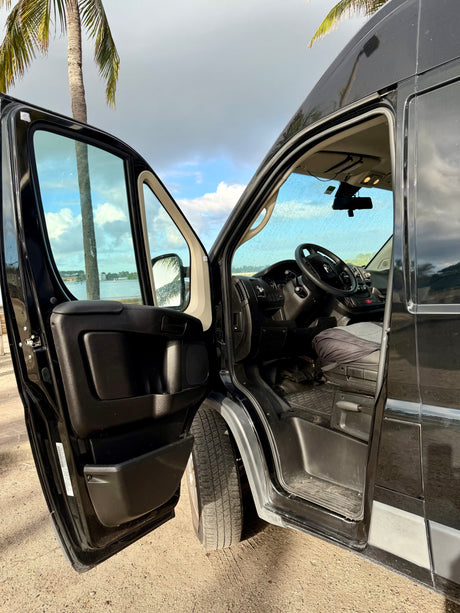 Open driver's door of an RV rental, revealing the interior cabin and a scenic view of a palm tree and water.