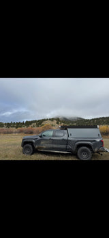 Rugged dark truck with pop-top camper in a cloudy mountain landscape. An ideal off-road adventure rv rental option.
