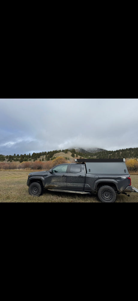 Rugged dark truck with pop-top camper in a cloudy mountain landscape. An ideal off-road adventure rv rental option.