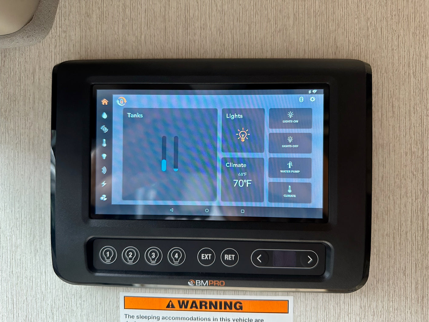 RV rental control panel showing tank levels, climate (68°F/70°F), and light settings with physical buttons below.