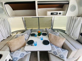 Inside an RV rental: a modern dinette with comfortable cushions, set table, and an integrated entertainment system.