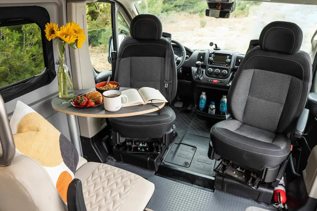 Swivel seats and a table set for breakfast with sunflowers and a book inside an RV rental camper van.
