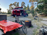 Enjoying an RV rental adventure: a red campervan parked at a campsite with a cozy fire, bike, and picnic table.