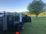 Explore off-road with this dark gray teardrop camper, perfectly set for an rv rental adventure amidst green hills.