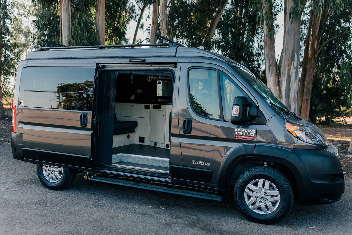 Dark gray Ram ProMaster Tofino camper van, perfect for an RV rental adventure, with its side door open showing the interior.
