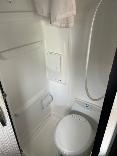 Compact white bathroom in an RV rental, featuring a toilet, shower hose, and hanging towel.