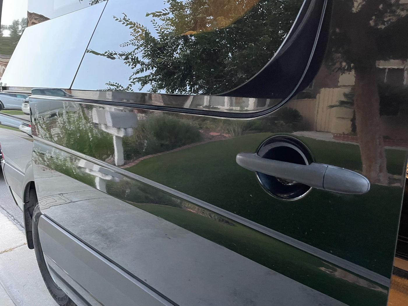 Side of a sleek, dark rv rental van with reflective windows and body showing clear reflections of suburban homes and trees. — photo 20