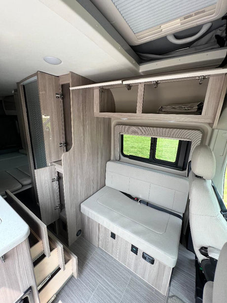 Modern rv rental camper van interior with convertible bench seating, open overhead storage, and a functional kitchen area, ideal for travel.