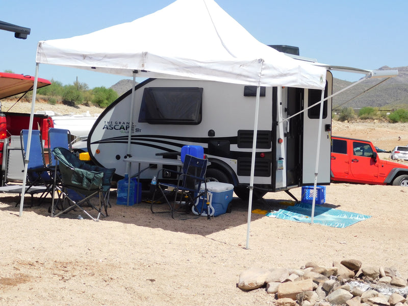A white teardrop RV, an ideal rv rental, is parked with a canopy, chairs, and a fire pit for comfortable desert camping. — photo 10