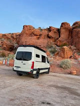 White camper van, perfect for RV rental adventures, parked on a dirt road amid stunning red rock formations.