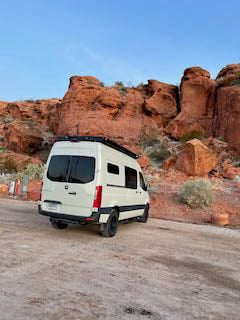 White camper van, perfect for RV rental adventures, parked on a dirt road amid stunning red rock formations.