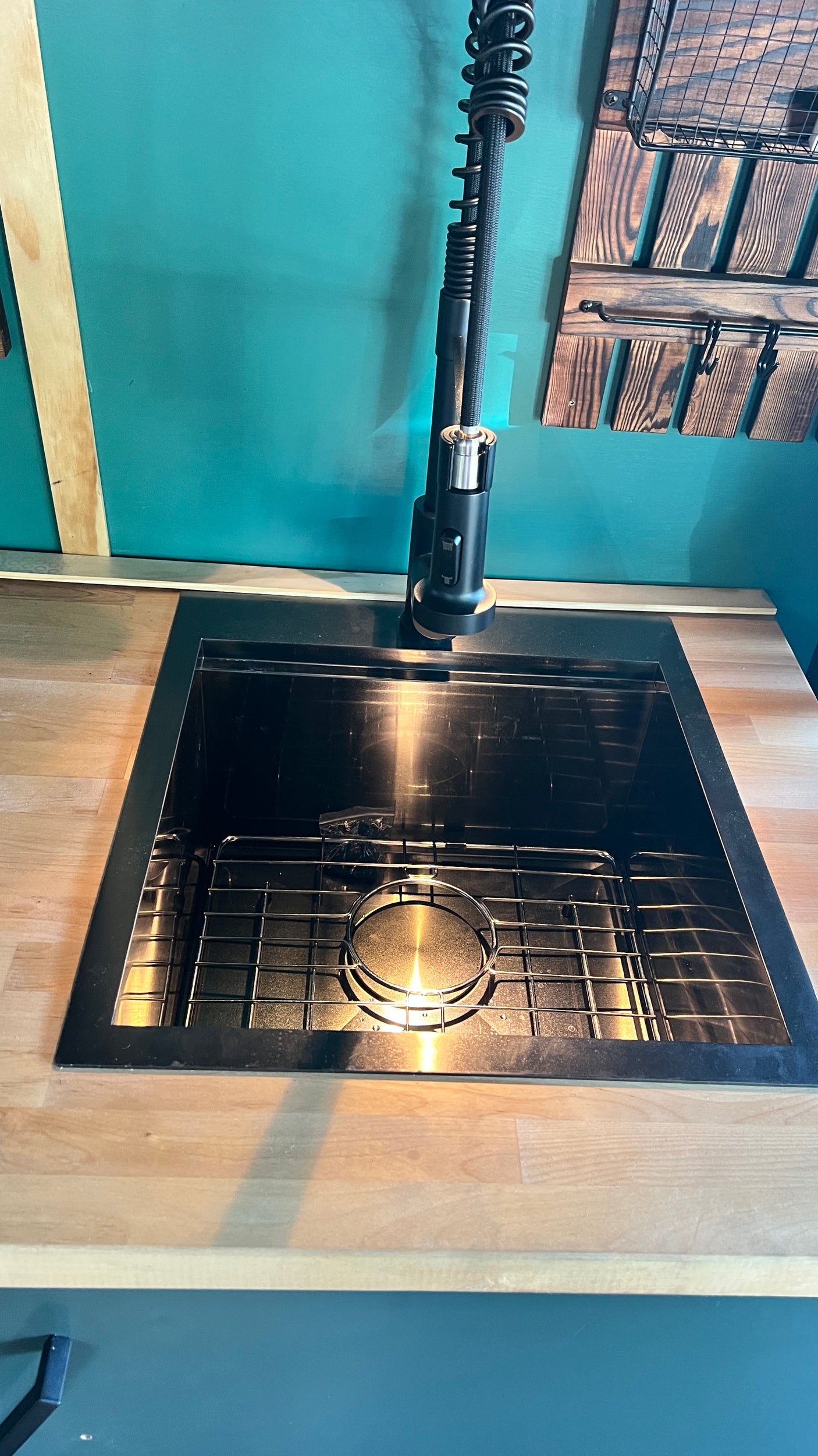 Close-up of a sleek black kitchen sink with a high-arc faucet in an RV rental unit. Features light wood counters and teal walls.