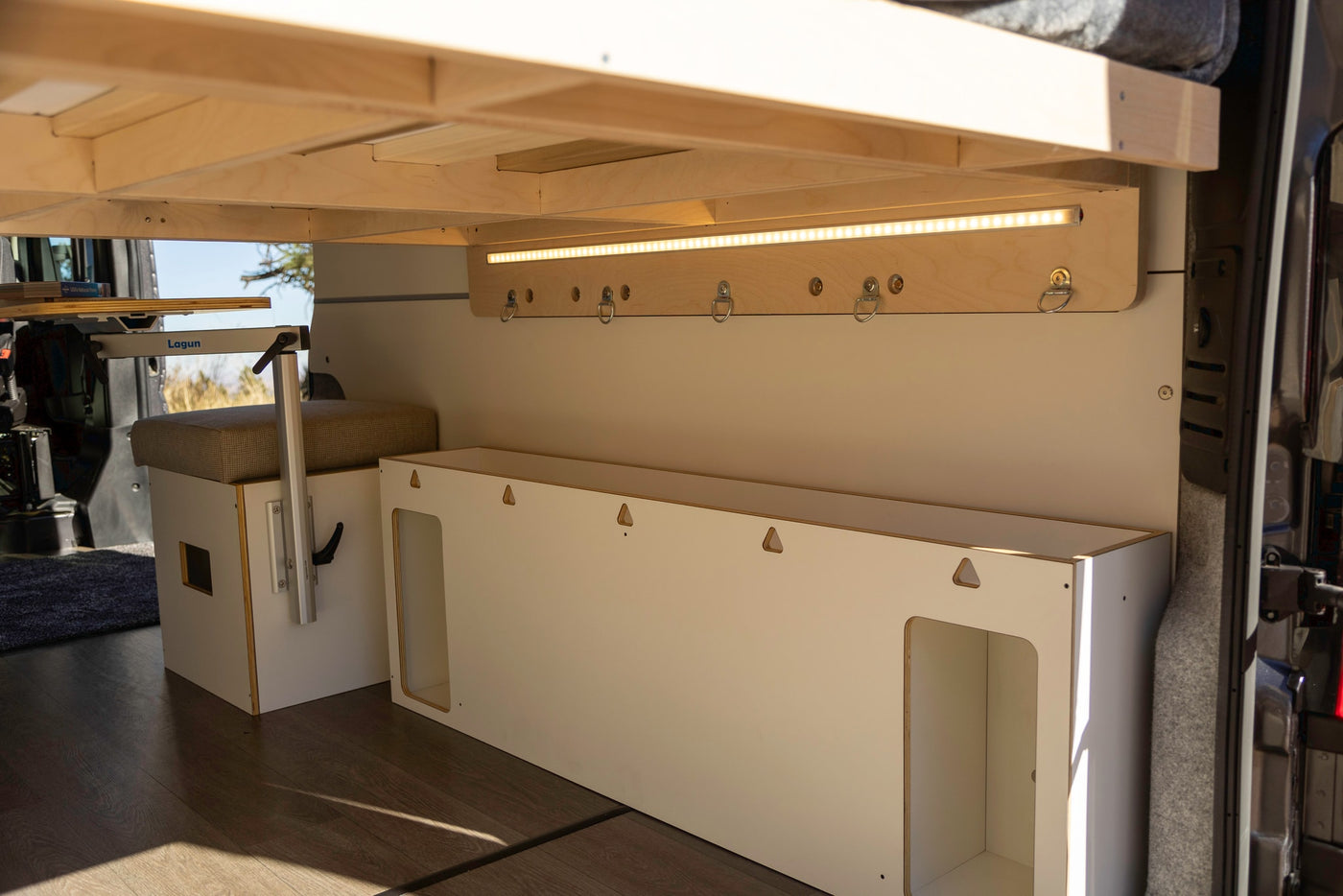 RV rental interior showing a wooden bed frame, versatile Lagun table, LED lighting, and modular storage solutions. — photo 10