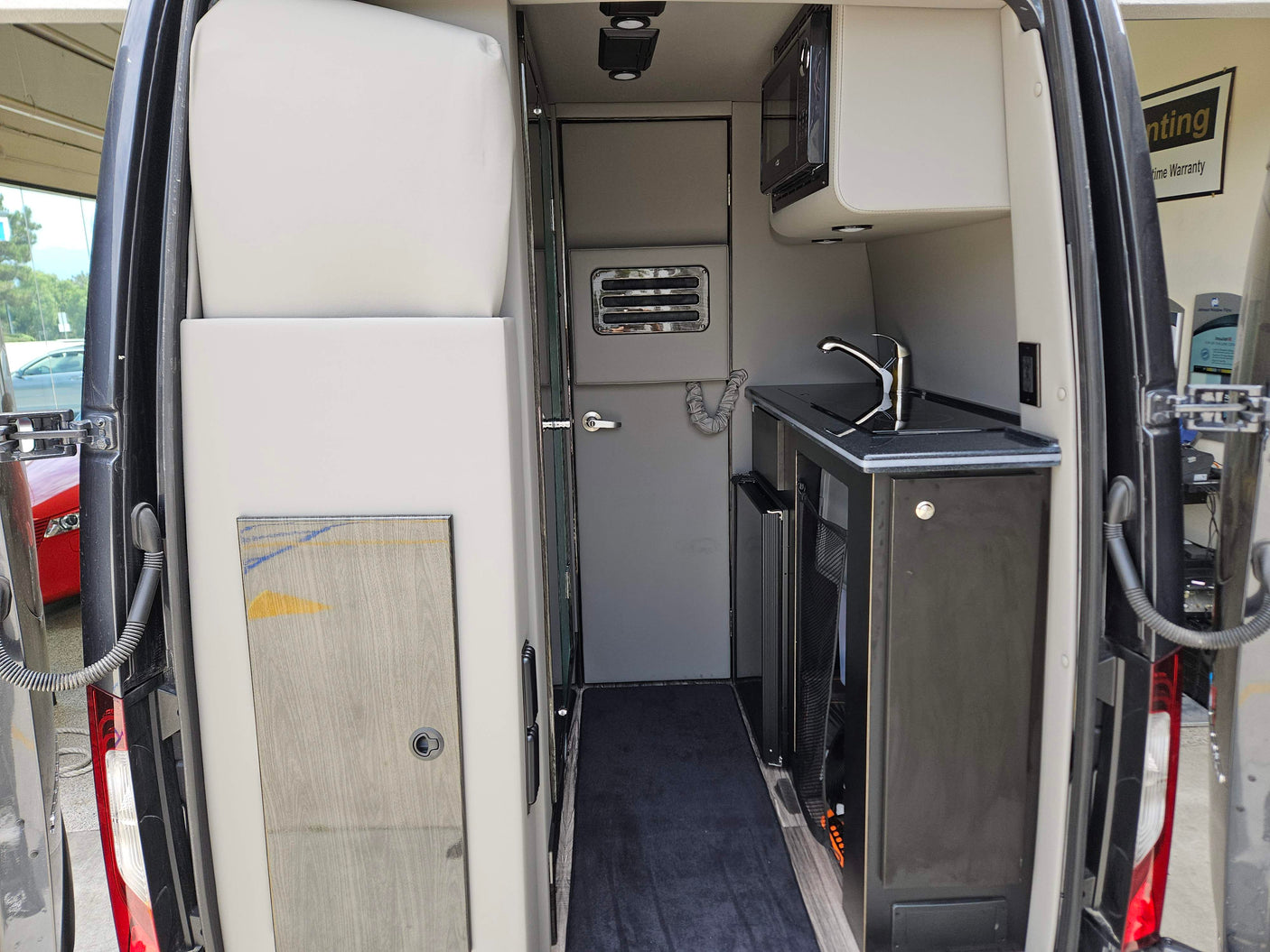 Interior of a modern RV rental. Features a compact kitchen with sink, microwave, and fridge on the right, and a sleeping/seating area on the left.