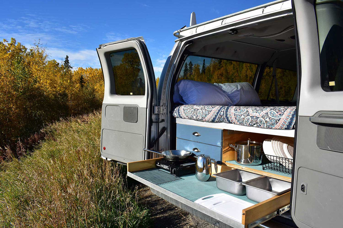 Cozy bed & pull-out kitchen in a custom camper van: perfect for your next outdoor RV rental road trip adventure!|This rv rental features a cozy bed above a pull-out kitchen with stove