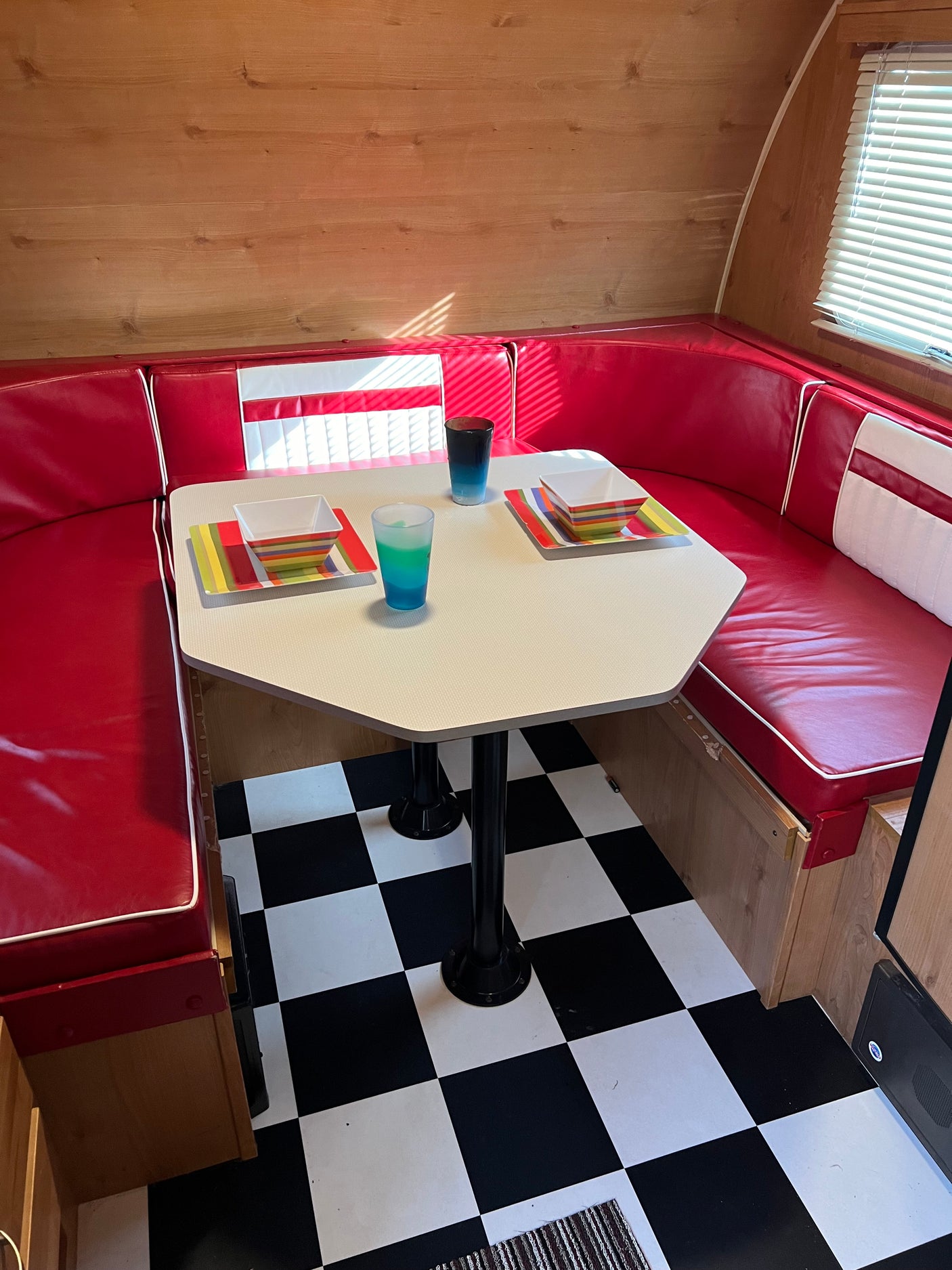 An RV rental interior with a retro red diner booth, octagonal table set with colorful dishes, and a black and white checkered floor.