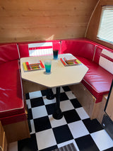 An RV rental interior with a retro red diner booth, octagonal table set with colorful dishes, and a black and white checkered floor.