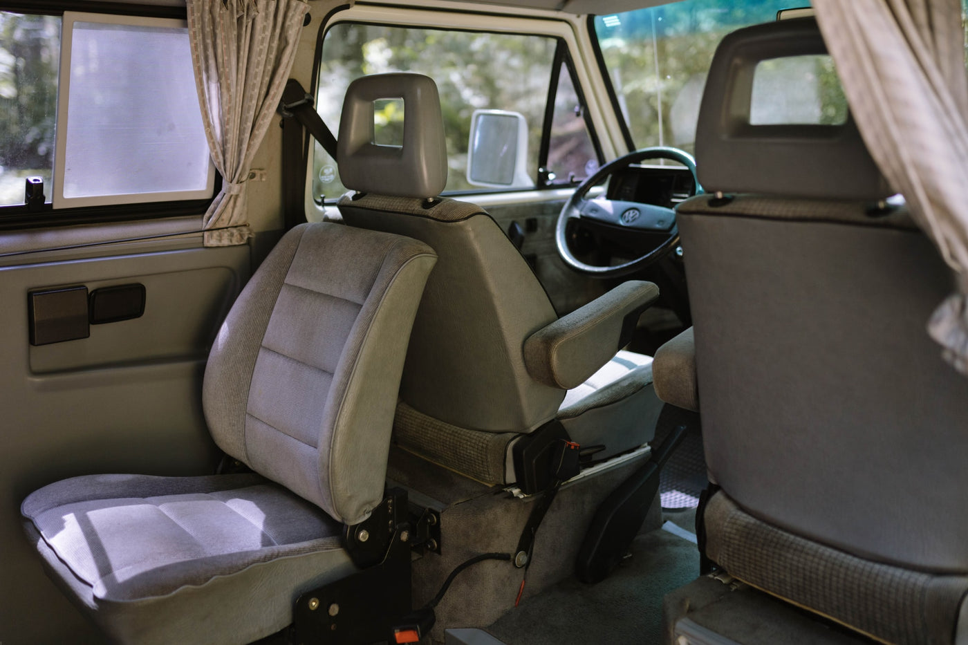  parked in a lush forest campsite with its pop-top and awning out.|A white camper van — photo 6