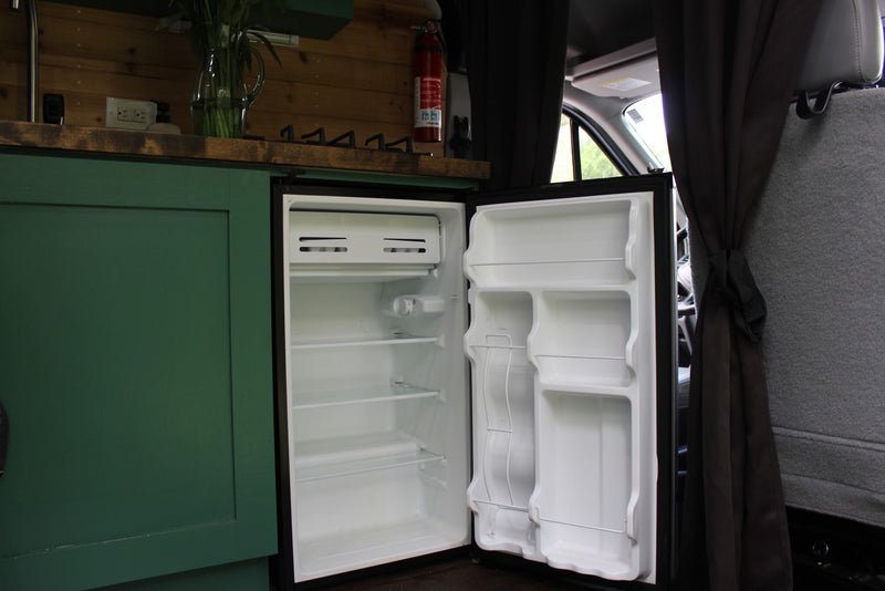 Empty mini-fridge in an RV rental camper van, showing shelves & door storage. Adjacent to a green cabinet, part of the vehicle interior. — photo 7
