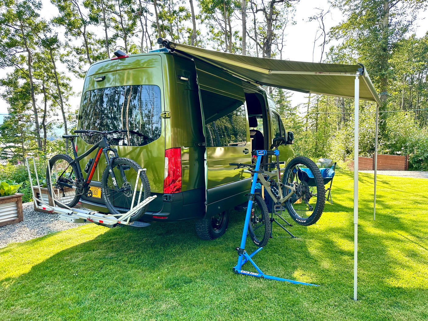 Green camper van with awning extended, bikes on rack & repair stand. An RV rental ready for adventure.