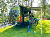 Green camper van with awning extended, bikes on rack & repair stand. An RV rental ready for adventure.