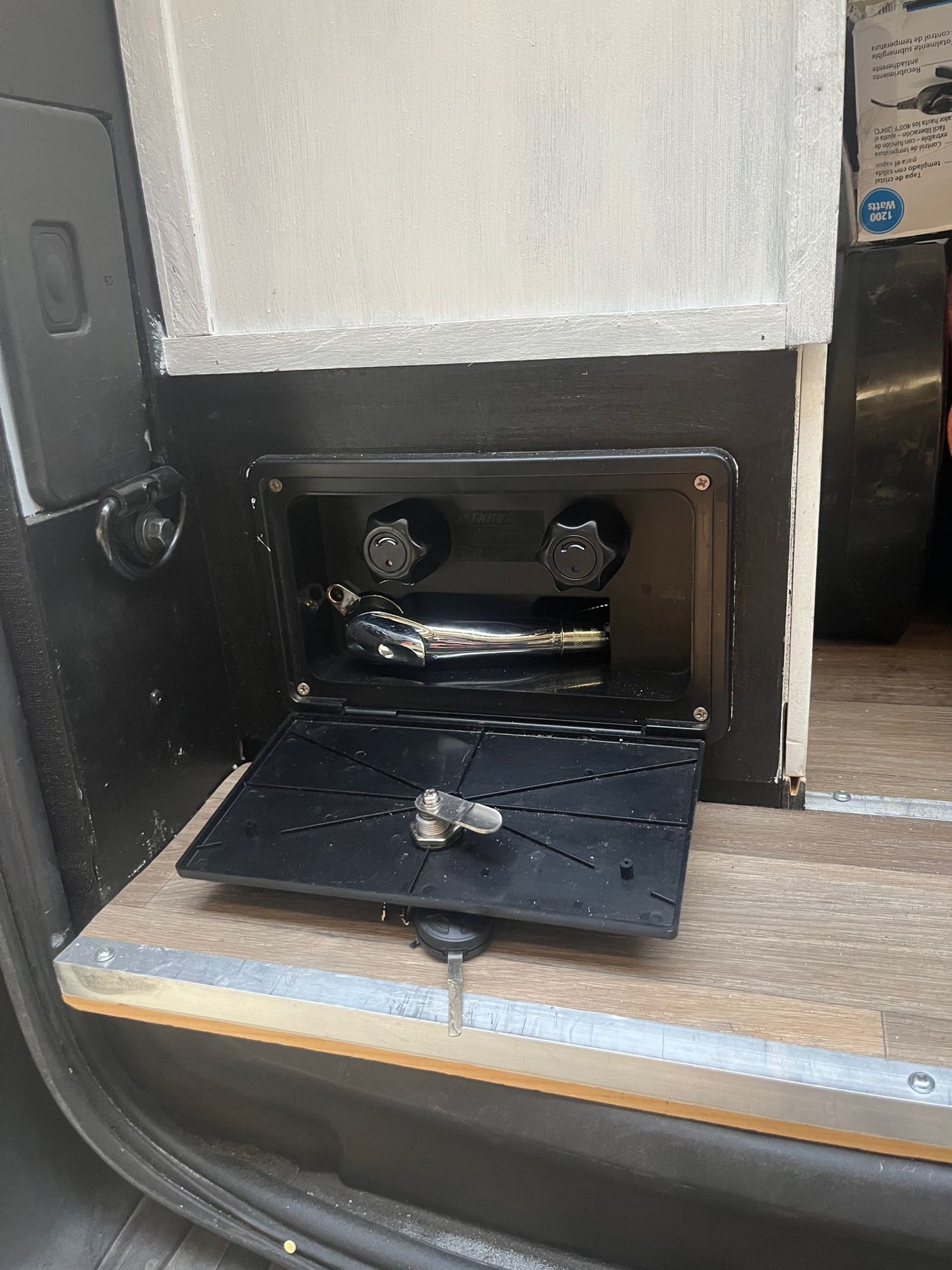 RV rental outdoor shower with chrome head and control knobs. Ready for use with its door open above wood flooring.
