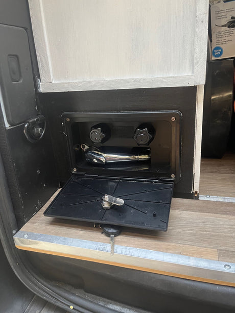 RV rental outdoor shower with chrome head and control knobs. Ready for use with its door open above wood flooring.