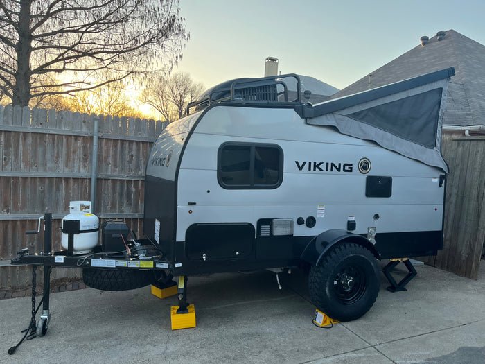 A gray and black Viking pop-up travel trailer, well-equipped for rv rental, parked on concrete with stabilizing jacks.