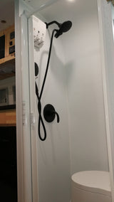 Modern RV rental bathroom: white shower stall with sleek black fixtures, wall dispenser, and compact toilet. Ideal for road trips.