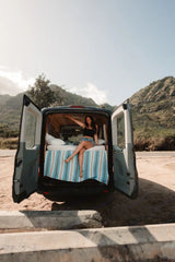 Woman enjoying her RV rental camper van bed, back doors open to scenic mountains. Perfect for van life road trips!
