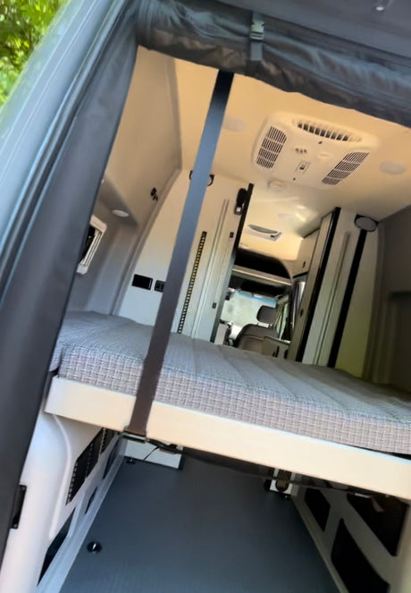 Inside a modern RV rental: a comfortable elevated bed with storage underneath, and overhead AC, perfect for mobile adventures.