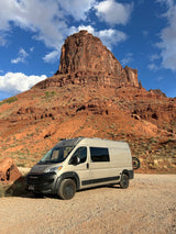 Explore stunning landscapes with an RV rental camper van parked at the base of a towering red rock mountain.