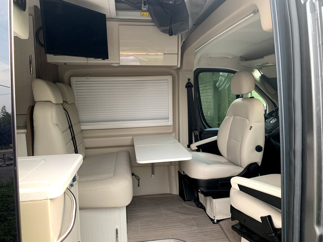 Interior of a modern RV rental showing light cream seating, an adjustable table, and a mounted TV for comfortable travel.
