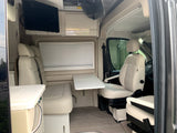 Interior of a modern RV rental showing light cream seating, an adjustable table, and a mounted TV for comfortable travel.