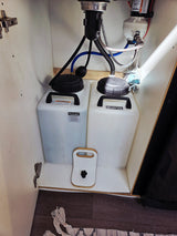 RV rental water system features a Flojet pump, fresh water jug, and wastewater holding tank under the sink.