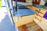 Functional kitchen area in this RV rental van, with sink, faucet, and integrated wood cabinetry.