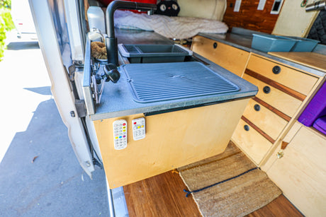 Functional kitchen area in this RV rental van, with sink, faucet, and integrated wood cabinetry.